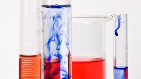 Graduated cylinders and a beaker filled with coloured chemical compounds in a laboratory