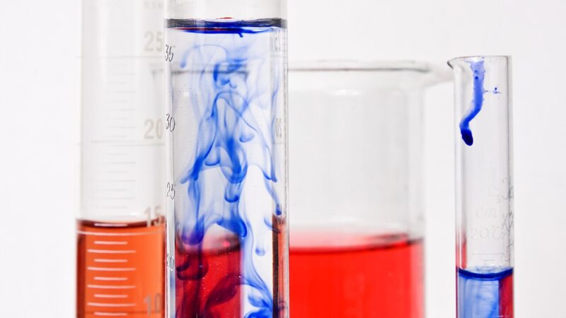 Graduated cylinders and a beaker filled with coloured chemical compounds in a laboratory