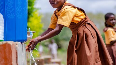 A school pupil washing her hands at an outdoor tap