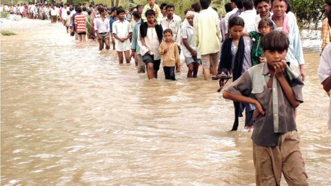 Villagers walking through floodwater toward dry ground during monsoon flooding