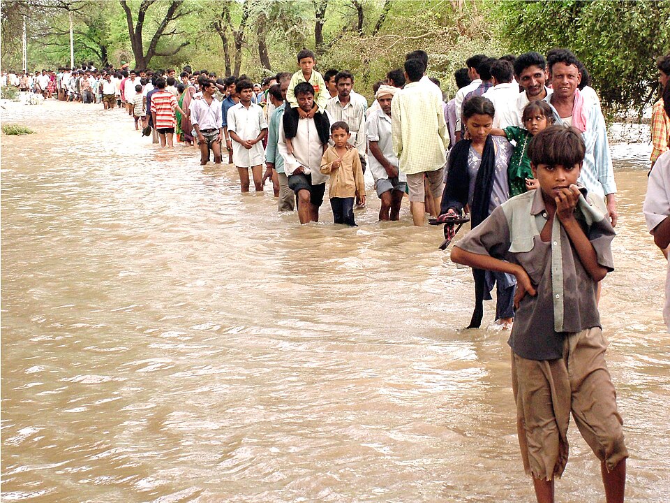 Villagers walking through floodwater toward dry ground during monsoon flooding
