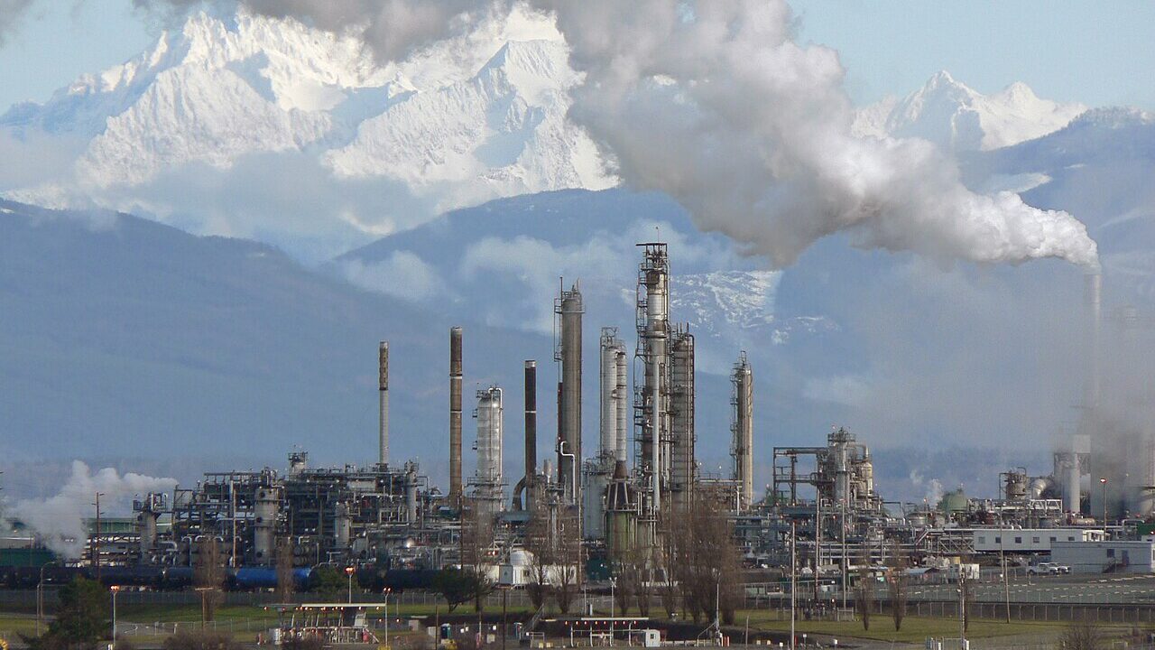 Oil refinery with steam rising against snowy mountains