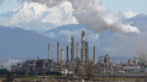 Oil refinery with steam rising against snowy mountains