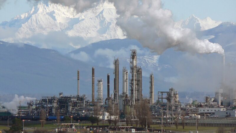 Oil refinery with steam rising against snowy mountains